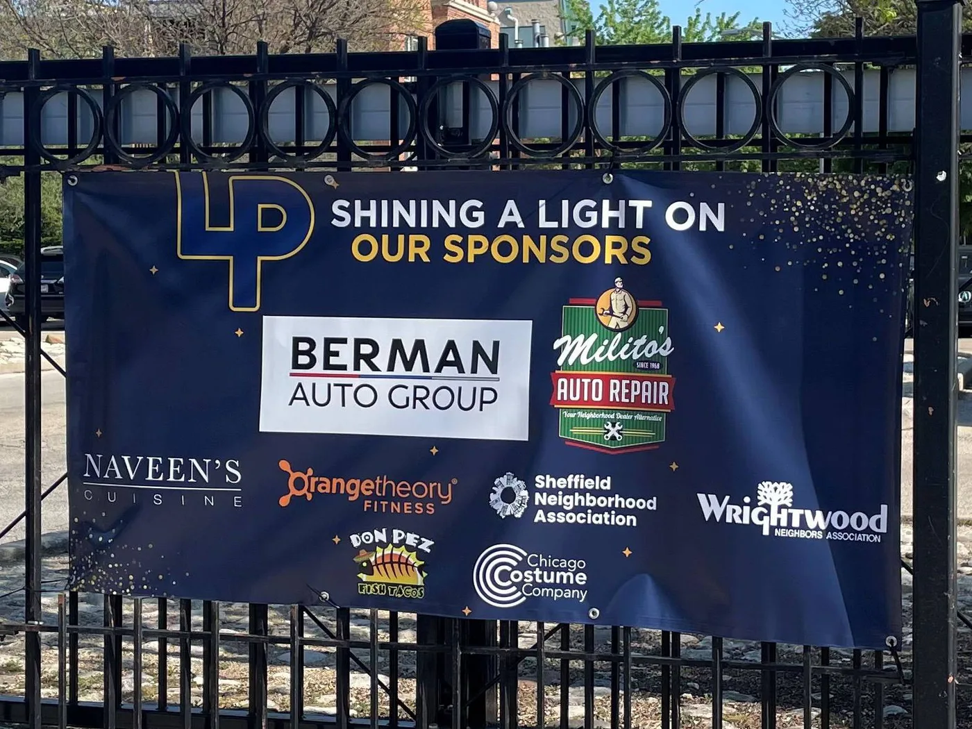 The 2025-26 FOLPHS sponsor banner on the Armitage St. fence at Lincoln Park High School, reading Shining a light on our sponsors with eight sponsor logos